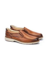 Zapatos de cuero marrón de tipo slip-on con un acabado suave, costuras en contraste y una suela de goma beige. Presenta un diseño de perfil bajo.