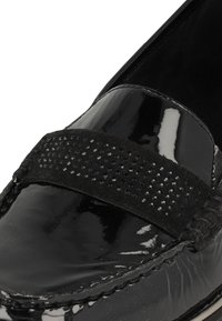 Zwarte gepatenteerde leren loafer met een zwarte suède band met kleine, glanzende studs. Gladde oppervlakte met tonale stiksels en gevlochten accenten.