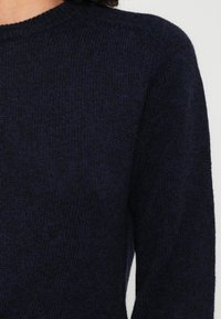 Mornarsko pleteno pulover z okroglim izrezom in dolgimi rokavi, ki se ponaša z teksturirano površino iz mehkega in gostega blaga.