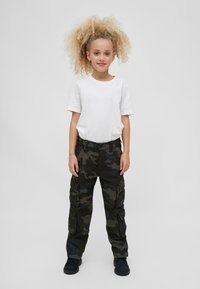 Vit kortärmad t-shirt kombinerad med mörka kamouflagebyxor med sidofickor, bärs med mörka skor. Enkel, avslappnad outfit.