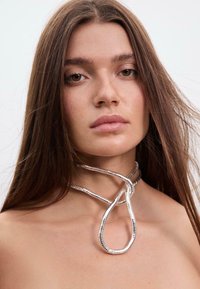 Collana choker d'argento con un design a cerchi, caratterizzata da una finitura metallica liscia e da sottili accenti testurizzati, delineata su pelle nuda.