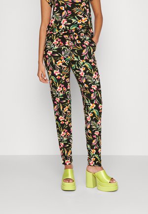Pantalons noirs à motifs floraux vifs en rose et vert, associés à des talons compensés verts et volumineux. Tissu doux et coupe ajustée.