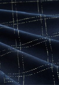 Tissu bleu foncé à texture douce présentant un motif de grille légère cousue formant des carrés et des rectangles irréguliers.