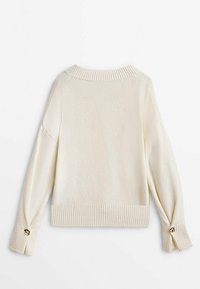 Pull en maille couleur crème avec un ourlet et des poignets côtelés, présentant des épaules arrondies et des accents de boutons métalliques sur les manches.