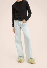 Light blue wide-leg jeans with a soft texture, paired with a black knit sweater. Footwear features green fur accents.