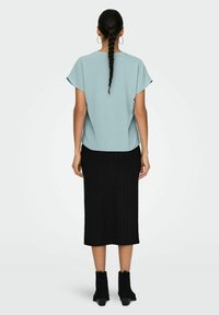 Top tejido azul claro con mangas cortas, combinado con una falda midi negra de canalé y botas de tobillo negras con tacón esculpido.