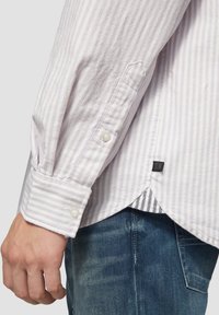 Lichtpaarse gestreepte langemouwen shirt met knoopmanchetten en een zijsplit aan de onderkant, gelaagd over een verticaal gestreept t-shirt. Spijkerbroek zichtbaar.