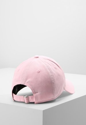 Casquette de baseball rose clair avec une sangle à boucle métallique réglable, posée sur une surface blanche sur un fond gris clair uni.