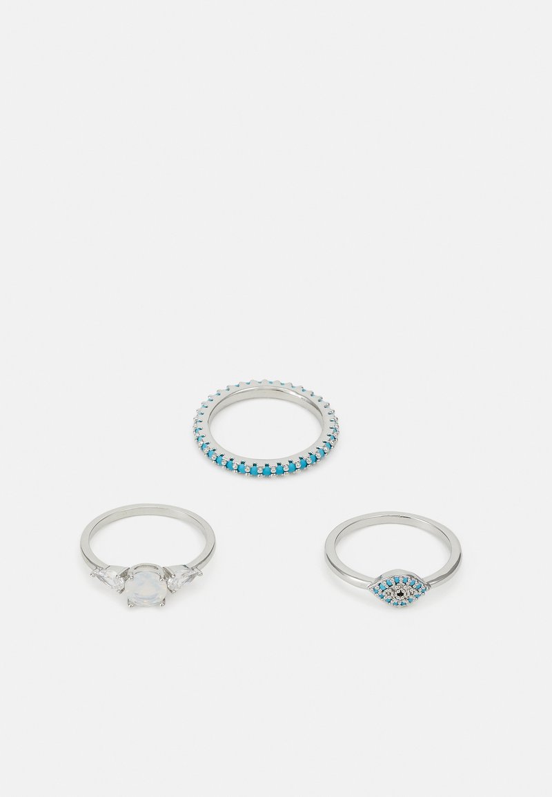 Trīs sudraba gredzeni: viens ar rindu zilo akmeņu, otrs ar centrālo caurspīdīgo akmeni, ko apņem divi mazi akmeņi, un trešais ar zila acs dizainu ar akcentiem.