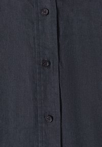 Tissu tissé gris foncé avec trois boutons noirs cousus verticalement sur la patte avant d'une chemise.
