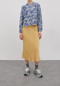 Blusa floreale a maniche lunghe blu e bianca, abbinata a una gonna midi gialla. Le sneakers grigie e i calzini grigi completano l'outfit.