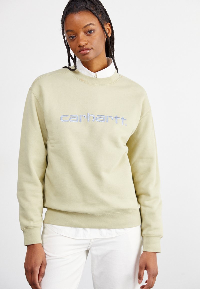 Lys grønn genser med høyt hals og ribbestrikkede mansjetter, med brodert "carhartt." logo i blått. Bært over en hvit skjorte med krage.