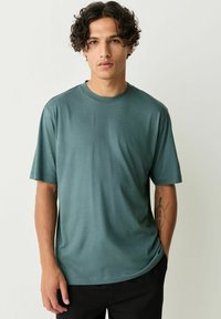 Tricou verde cu mânecă scurtă, dintr-un material neted, cu guler rotund și croială lejeră. Design minimalist, fără modele sau accente vizibile.