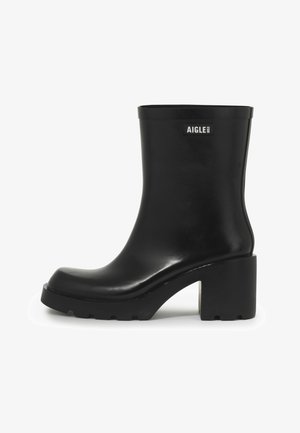 Botte de cheville en caoutchouc noir avec un talon épais, bout rond, finition lisse et un accent logo sur le côté extérieur. Semelle texturée pour une meilleure adhérence.