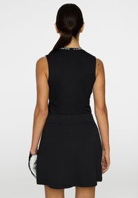 Svart ärmlös klänning med en figursydd överdel och utsvängd kjol. Har en subtil textur, med logotyp vid halsringningen och stiliga detaljer.