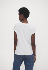 Witte t-shirt met korte mouwen, ronde hals en een gladde textuur, gecombineerd met blauwe denim jeans met stikseldetails op de achterzak.