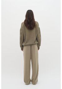 Olivovo zelený pletený sveter s voľným, open weave dizajnom; skombinovaný s béžovými, voľne strihanými nohavicami z hladkej tkaniny.