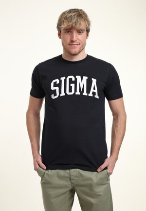 Sort t-shirt med hvid "SIGMA" tekst tværs over brystet, rund halsudskæring og korte ærmer. Parret med lysegrønne bukser.