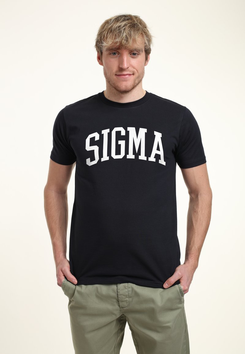 Camiseta negra con texto blanco "SIGMA" en el pecho, con cuello redondo y mangas cortas. Combinada con pantalones verde claro.