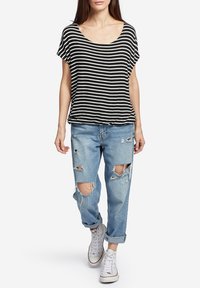 Top de manga corta a rayas en blanco y negro combinado con jeans de mezclilla claros desgastados y zapatillas blancas. Ajuste casual y relajado.