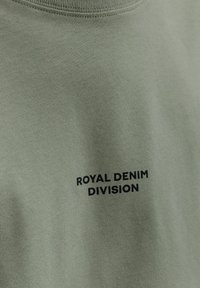Olivgrünes Baumwoll-T-Shirt mit Rundhalsausschnitt, auf der Vorderseite mit dem Text "ROYAL DENIM DIVISION" in fettem Schwarz bedruckt.