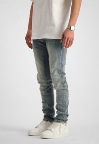 Lichtblauwe jeans met een slim fit, met vervagingsdetails. Gecombineerd met witte sneakers en een kortom mouw, off-white t-shirt.