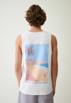 Ung person med kort krøllet hår bærer hvid ærmeløs skjorte med strandmotiv med palme, surfer og teksten "LONG SUMMER SURF."