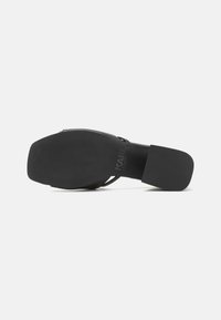 Sandale à talon noir avec un dessus en cuir lisse et une semelle en caoutchouc texturé. Détail de logo notable sur la semelle intérieure. Design moderne et minimaliste.