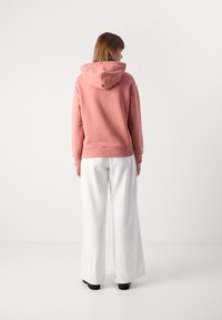 Felpa rosa con cappuccio dal taglio rilassato, abbinata a pantaloni bianchi a gamba larga. Il tessuto sembra morbido con dettagli a coste sui polsini e sull'orlo.