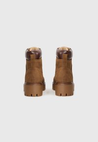 Bottines en daim marron avec des accents en cuir, col rembourré et semelle épaisse à motif. Présente une languette à l'arrière pour un enfilage facile.