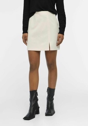 Vit miniskirt med en framspalt, tillverkad av mjukt tyg. I kombination med svarta läderankelboots med fyrkantig tå och stilettklack.