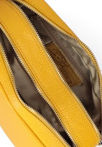 Borsa gialla in pelle con numerosi scomparti con zip e una superficie texturizzata. L'interno è foderato in tessuto marrone, che mostra l'etichetta del marchio.