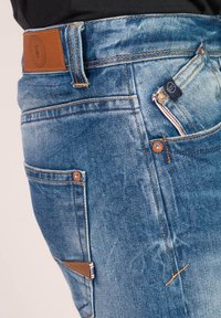 Lichtblauwe denim jeans met een leren patch bij de taille, contrasterende stiksels, vijf zakken en metalen hardware accenten.