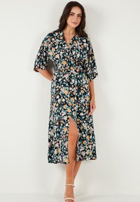 Floral maxi dress with a navy base, short kimono sleeves, and a side slit. Features orange and teal flower patterns throughout.