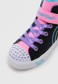 Sorte, glitrende høye sneakers med rosa og lilla detaljer. Har rhinestones på tåhetten og livlige snørebånd. Merkenavn synlig.