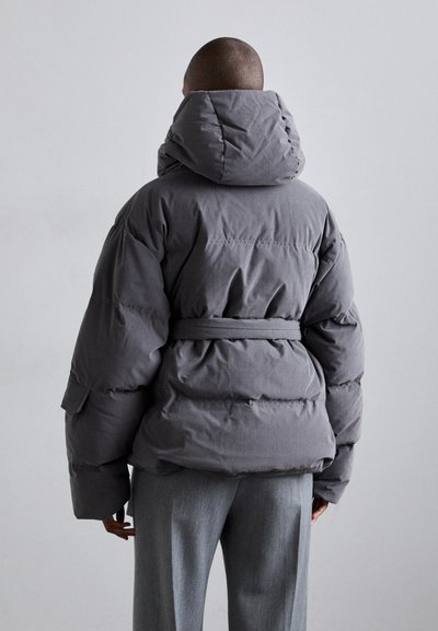 Puffy gray coat with a hood, belted waist, and large sleeves. Features a smooth texture and visible stitching. Styled with gray trousers.