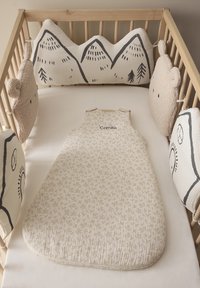 Kinderbett mit beiger Bettwäsche in Blattmuster. Rundum gepolsterte Bettumrandungen in Form von Bergen und Bären aus weichem Material.