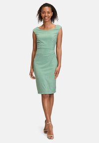 Robe verte ajustée avec un décolleté bateau, en tissu texturé, et longueur genoux. Accentuée de rayures horizontales, associée à des chaussures à talons argentées.