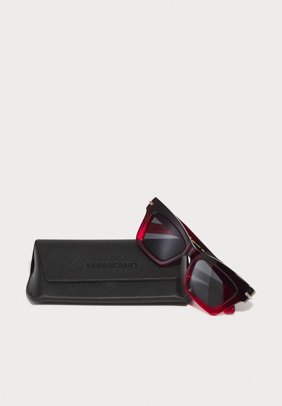 Musthave musta tekstuuriga prillikarp, millel on "FERRAGAMO" logo. Punase gradatsiooniga päikeseprillid ruudukujuliste raamidega ja tumedate läätsedega, millel on kuldsed aksesuaarid.
