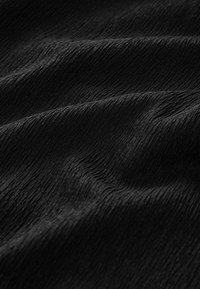 Zwarte textuurstof met subtiele golvende patronen, met een zachte en gladde uitstraling, die verschillende lichtreflecties vastlegt.