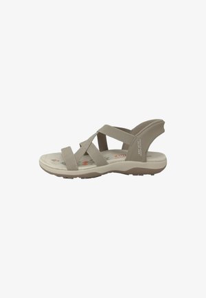 Sandal de color beige claro con correas cruzadas, plantilla acolchada, suela texturizada y sutiles acentos estampados en la plantilla.