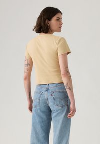 T-shirt a maniche corte, tagliata, in cotone giallo chiaro, design aderente, texture liscia, abbinata a jeans in denim blu chiaro a vita alta.