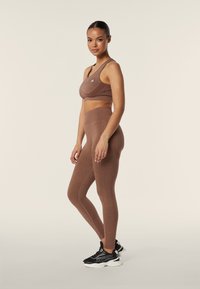 Set sportivo marrone composto da un crop top aderente e leggings a vita alta, realizzato in materiale liscio con cuciture e un dettaglio del logo.