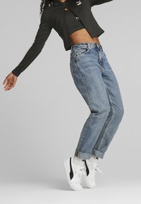 Chaqueta negra con cremallera, top corto, jeans de mezclilla azul claro, remangados en los tobillos, zapatillas blancas con detalles negros, tela texturizada.