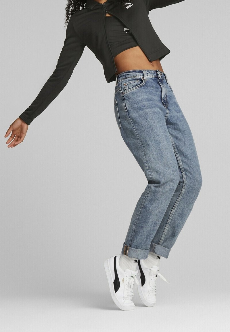 Chaqueta negra con cremallera, top corto, jeans de mezclilla azul claro, remangados en los tobillos, zapatillas blancas con detalles negros, tela texturizada.