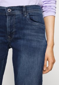 Jeans in denim blu scuro con taglio dritto, dotati di tasche frontali, chiusura con bottone metallico e dettagli di cucitura visibili.