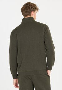 Tummanvihreä, ribatoitu villapaita korkealla kauluksella ja pitkillä hihoilla. Pehmeä pinta, jossa on rento malli ja elastinen vyötärö.