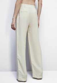 Pantalones de pierna ancha en tejido beige claro, con una textura suave, dos bolsillos traseros y un diseño de cintura alta.