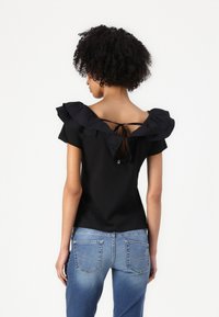 Top nero con scollatura ampia e arricciata e schiena scoperta, fissato con legature. Abbinato a jeans di media tonalità con tasche posteriori dettagliate.