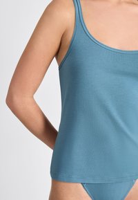 Hellblaues Tanktop mit Rundhalsausschnitt und dünnen Trägern, das eine glatte Textur und einen geraden Saum aufweist.